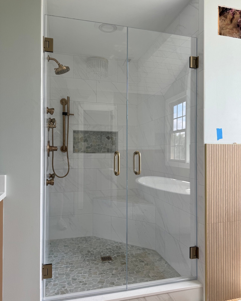 Frameless hinged shower door with inline panel and brushed gold hardware in a Maryland bathroom
